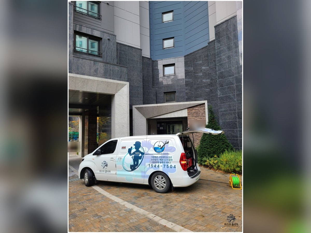 아파트 출입구 앞에서 작업 차량 뒷문을 열고 온수고압세척 작업을 준비하는 모습